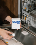 CUBE Dish box, up to 32 loads, held over an open dishwasher as a cube goes into the dispenser